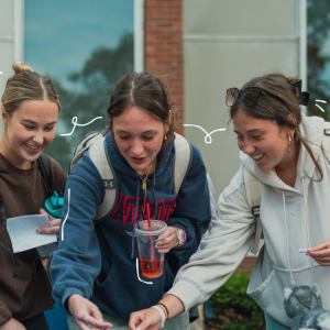 Three students laugh together while browsing items at an outdoor table, with playful hand-drawn accents around them."