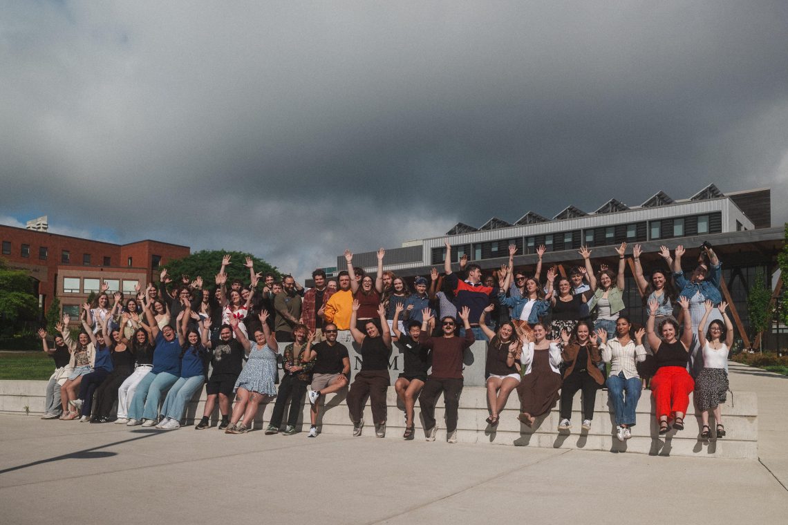 Large group of USM RAs and orientation leaders posing with raised hands on campus
