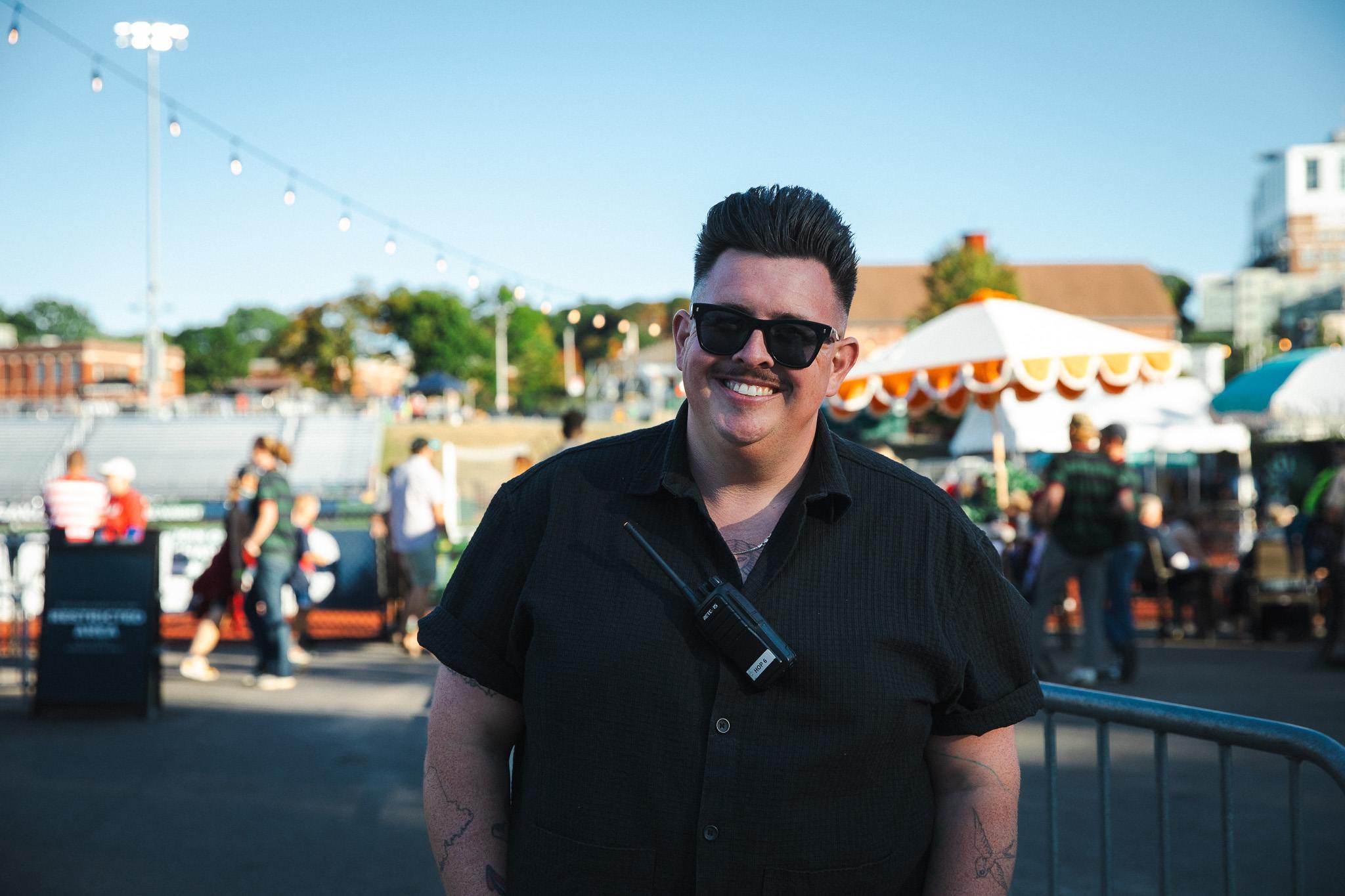 Kevin Oates, wearing sunglasses and a Hearts of Pine radio, smiles outside Fitzpatrick Stadium.