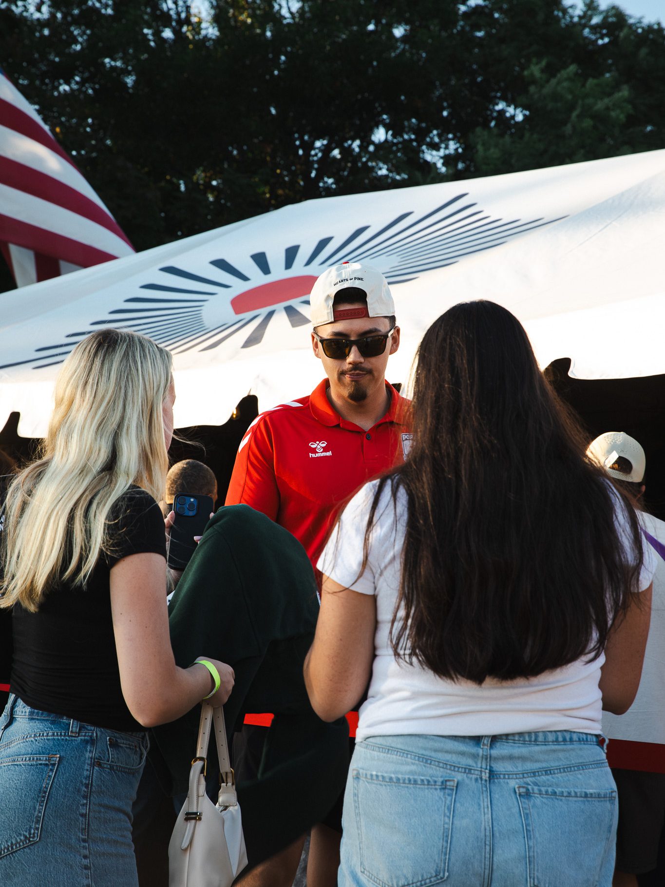 Chris Decker, wearing a Hearts of Pine polo, talks with fans at a merchandise tent before a match.