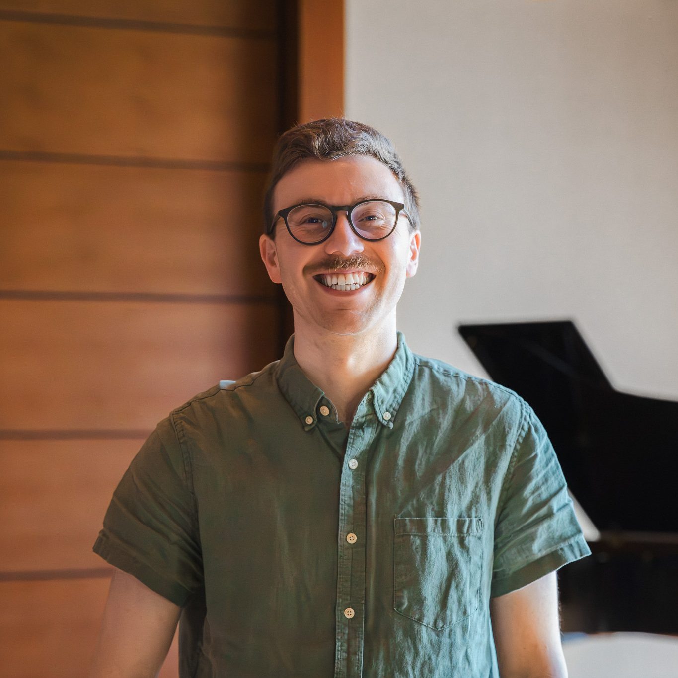 Sam Kyzivat smiles in front of a grand piano in the Crewe Center for the Arts.