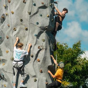 USM students climb a rock wall together outdoors during Fall Fest, part of Homecoming Weekend.