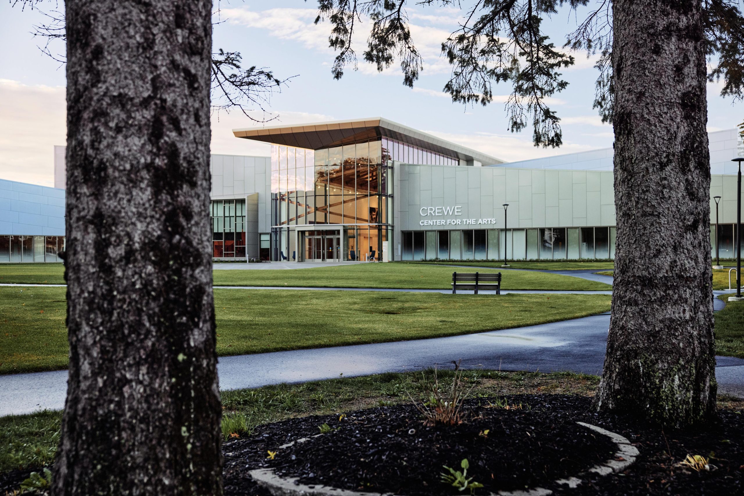 The exterior of the Crewe Center for the Arts on USM's Portland campus, viewed through pine trees at dusk.