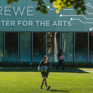 A student walks in front of the Crewe Center for the Arts on USM's Portland campus, with an illustrated circuit board graphic overlaid on the building exterior.