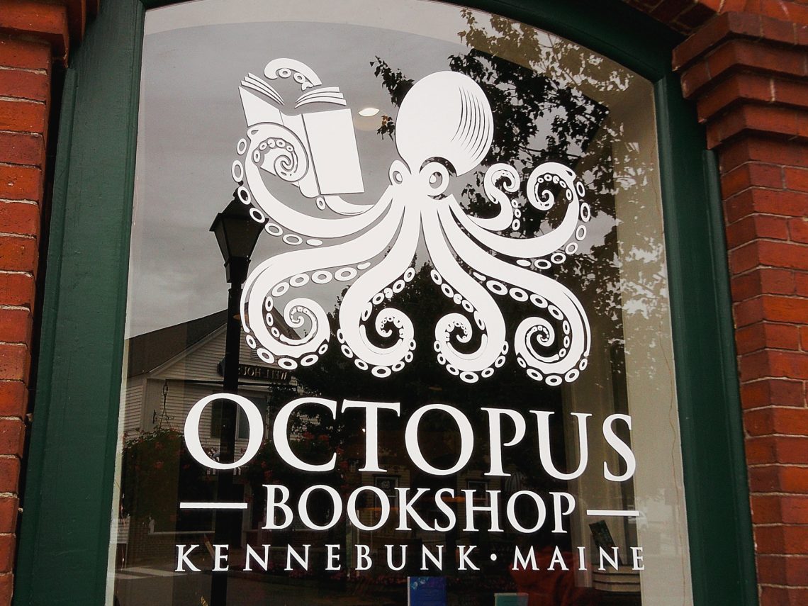A storefront window at Octopus Bookshop in Kennebunk, Maine, decorated with a white octopus logo holding an open book in one tentacle.