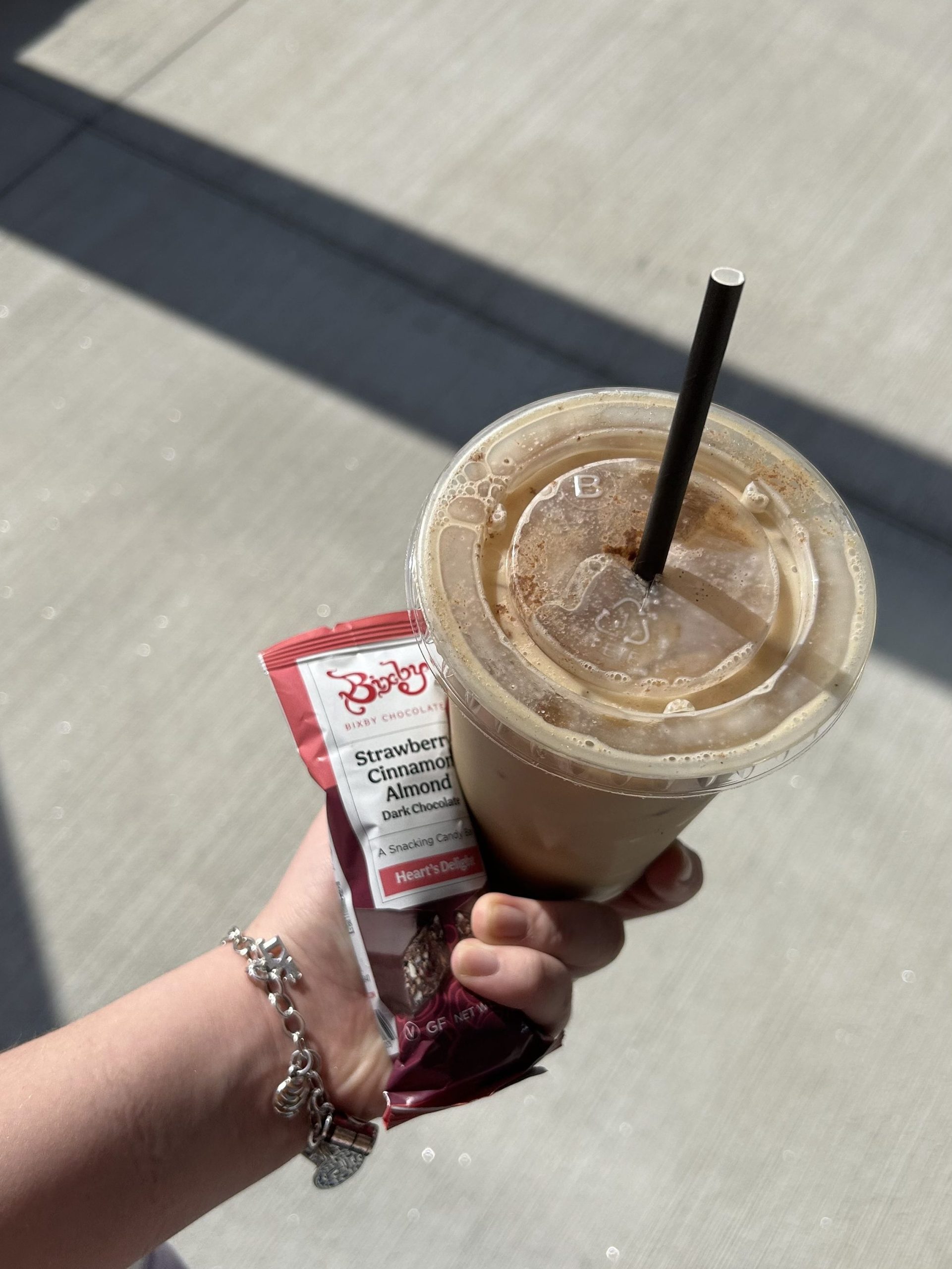 A hand holds an iced latte topped with cinnamon and a Bixby Strawberry Cinnamon Almond dark chocolate bar from the Husky Brew on USM’s Portland campus.