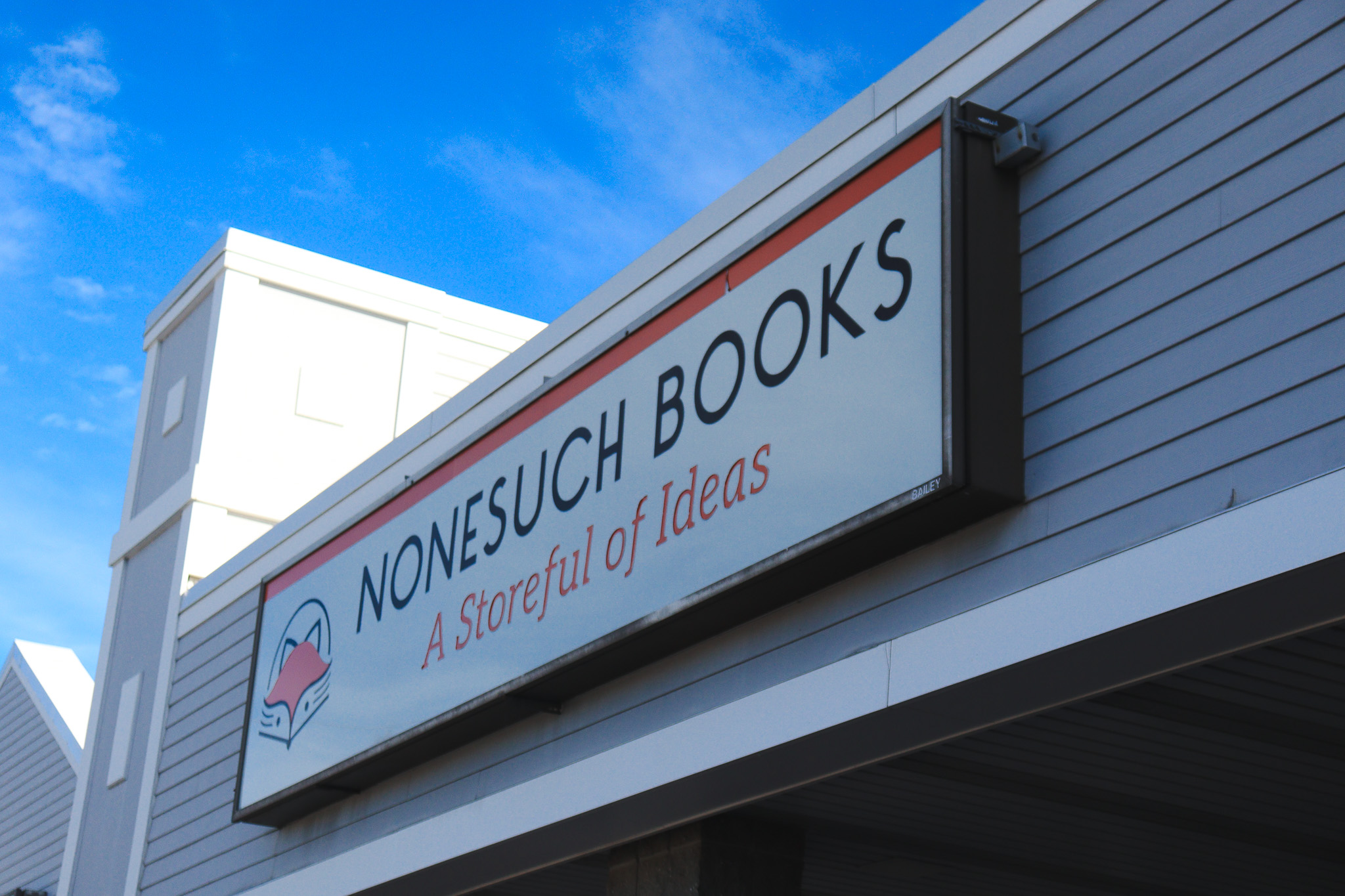 The exterior sign for Nonesuch Books, reading “A Storeful of Ideas,” against a bright blue sky.