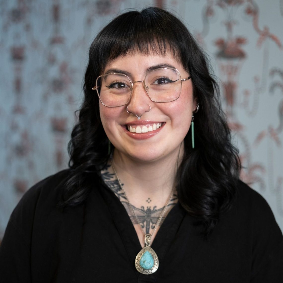 Marissa Joly smiles at the camera in glasses and a black top, with a turquoise pendant necklace.