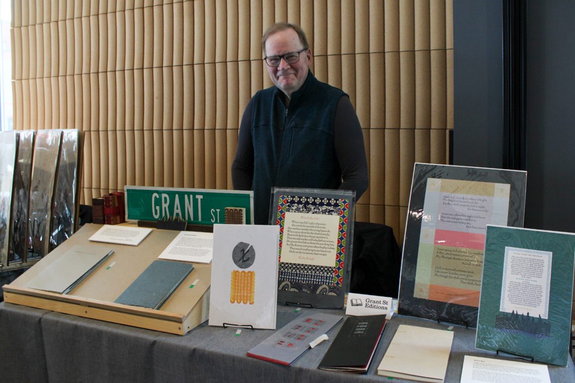 Walter Tisdale smiles behind his vendors table exhibiting handmade books, original prints and more.