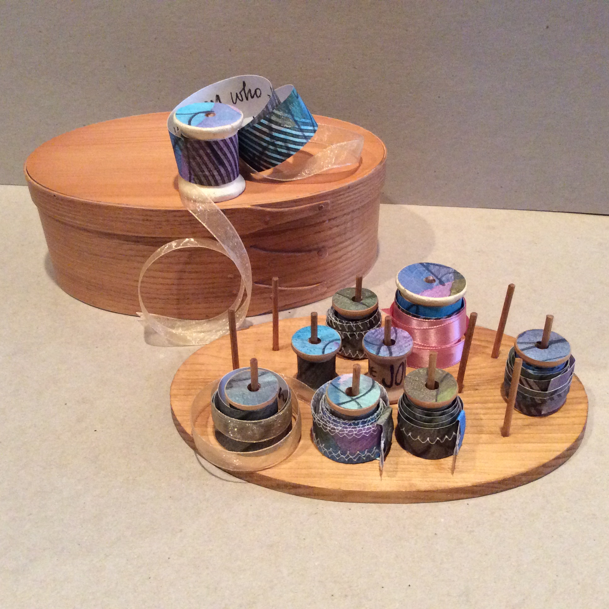 An image of artist book, "The Journey's Angst" by Bonnie Faulkner: made out of wooden rounded box, and ribbons as books.