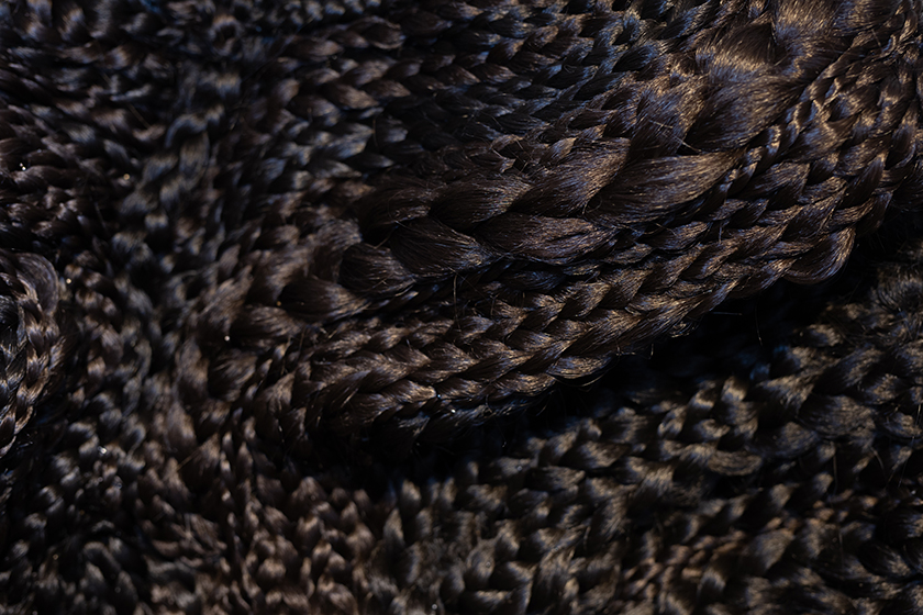 A close up of hundreds of braids of black artificial hair in varying thicknesses