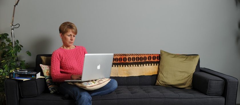 Person sits on a couch with a computer in their lap