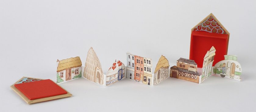 Folded paper art open and standing freely. Series of 8 different houses linked together like paper dolls.