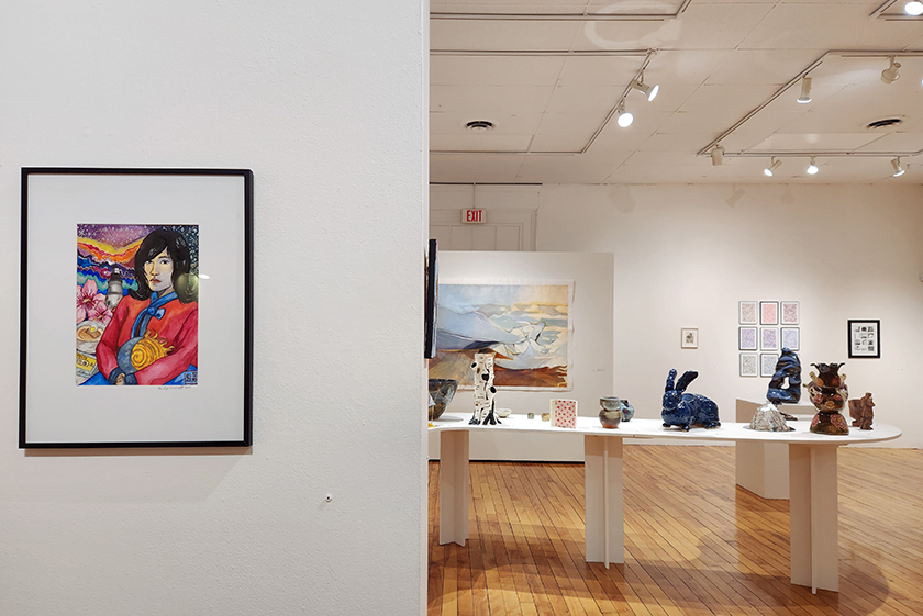 An image of an art gallery with a watercolor portrait in the foreground and a table of sculptures in the background.