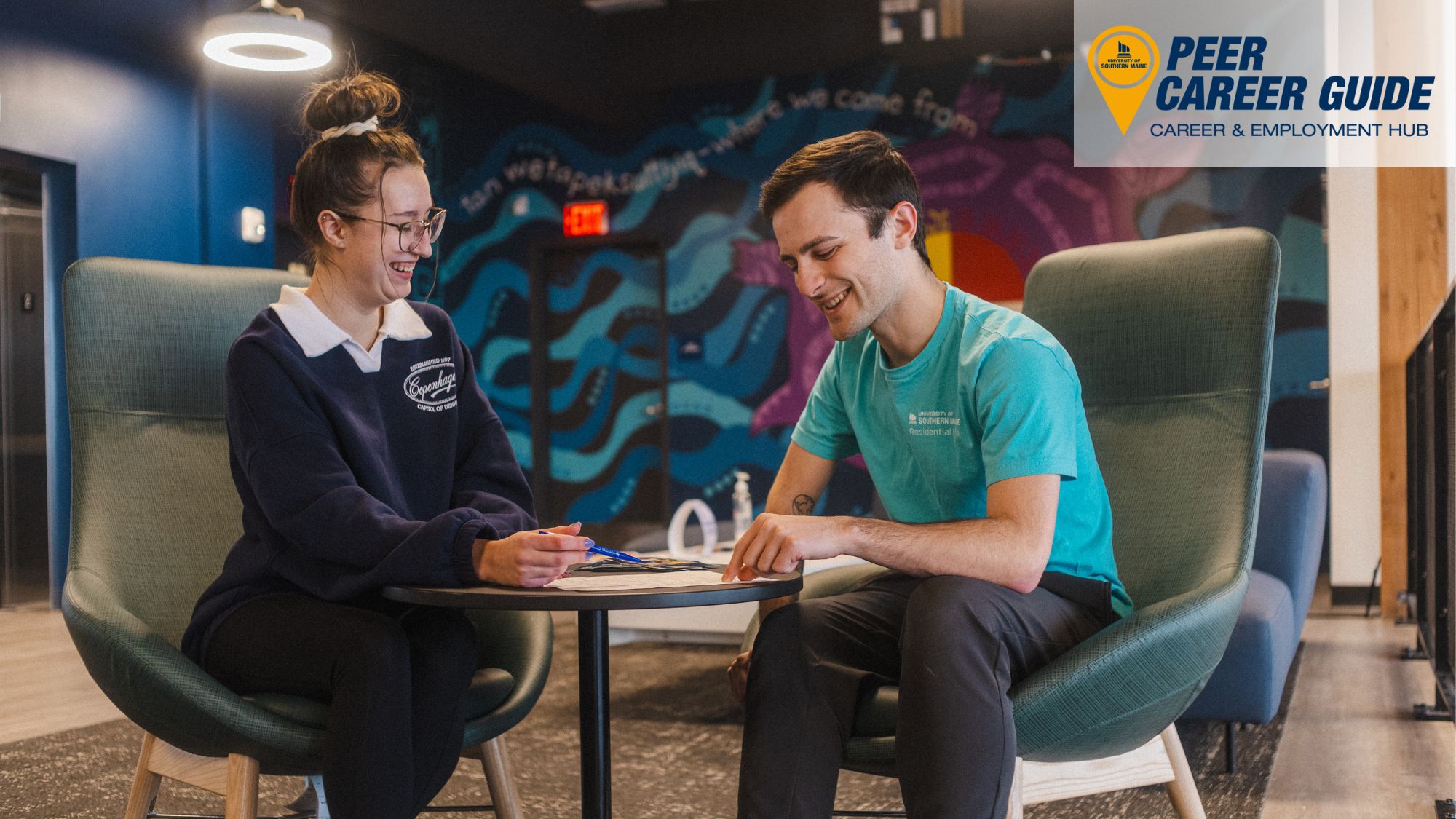 Two students sit in McGoldrick looking at a resume together. Peer Career Guide logo is in the corner.