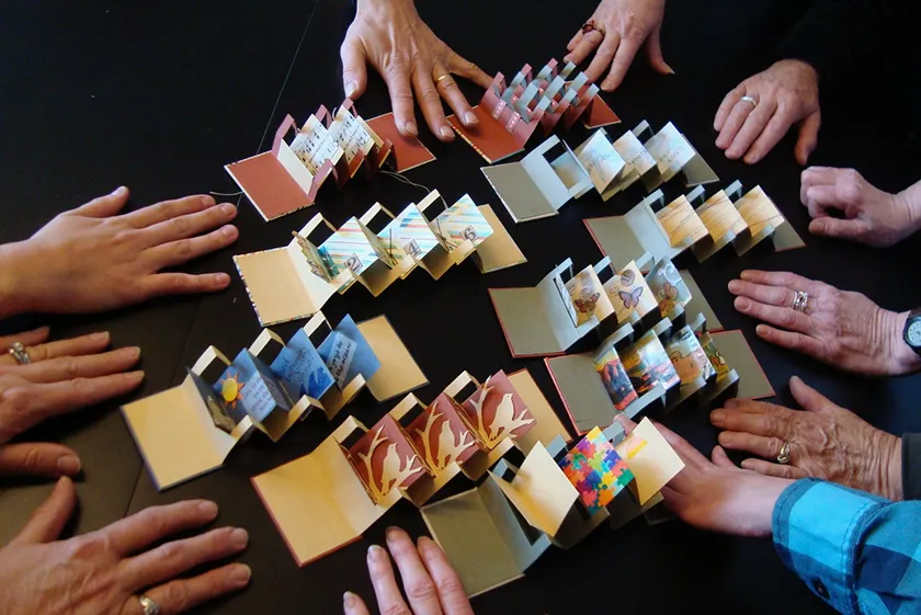 A group of 10 miniature books is surrounded by 11 hands to illustrate scale.