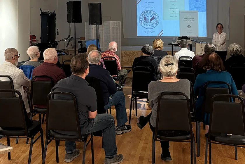 A group of people sitting in a large room facing a projected presentation.