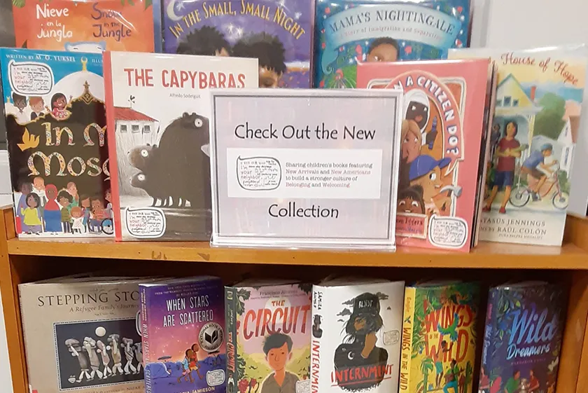 A bookshelf display of a variety of children's books and a sign to "check out the new collection."