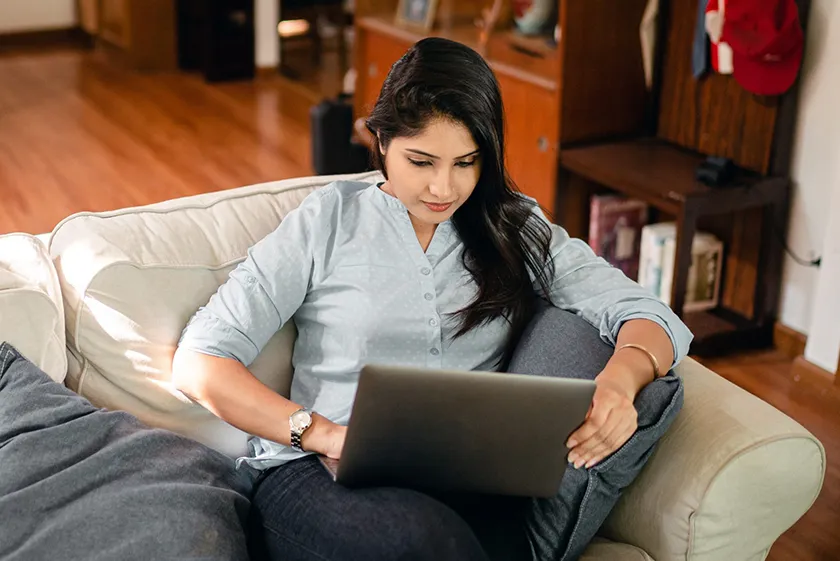 A student is seated on a light-colored couch with a laptop.