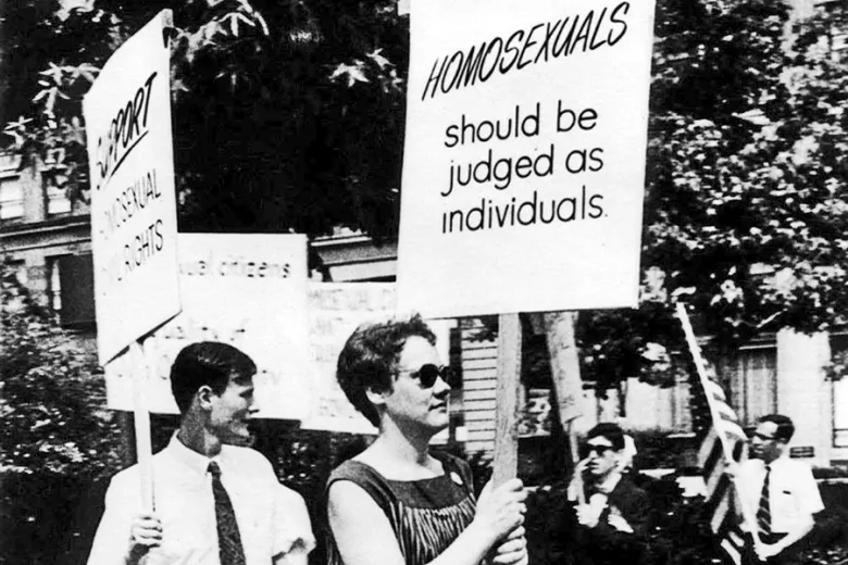 Black and white image of protestors from 1965. One sign reads, "Homosexuals should be judged as individuals."