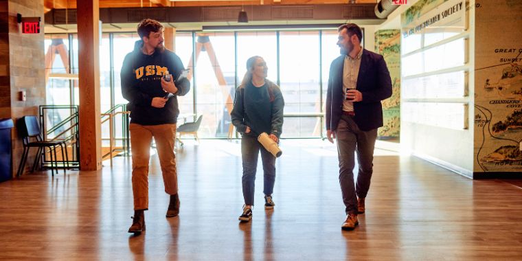 Three members of the USM community walk down the hall in the McGoldrick Center to each other.