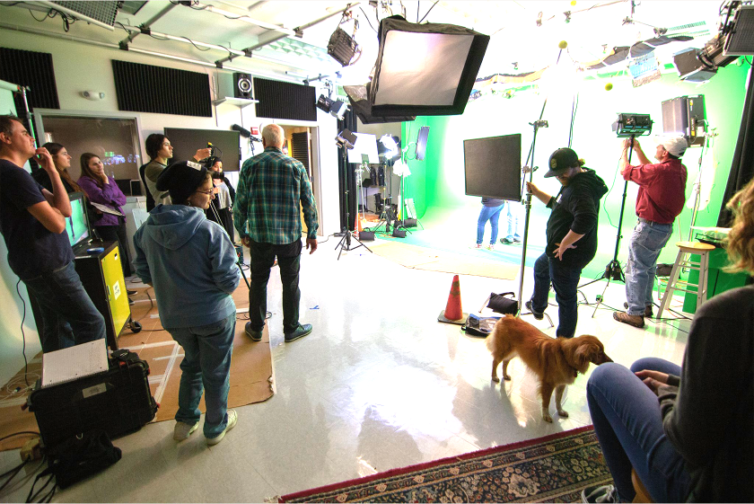 A group of video production studets and a dog gather around a green screen