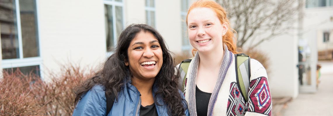 Two students standing in front of a building together, smiling.