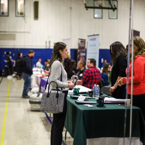 A student standing in front of an employer table talking to a representative at the Job Fair