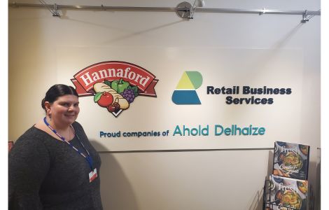 Catherine Mallory, '24, standing in front of Job Shadow Host Site Hannaford Logo