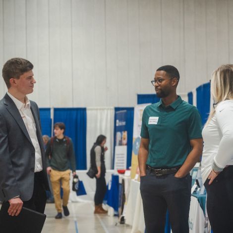 A student talks with two employer representatives in the Sullivan Gym during the Job & Internship Fair