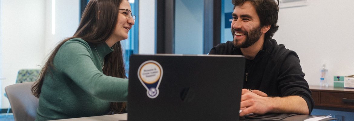 Two students talking to each other with an open laptop on the table.