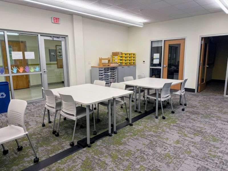 Two clusters of desks with chairs and in the background there is supplies from the maker space room. 