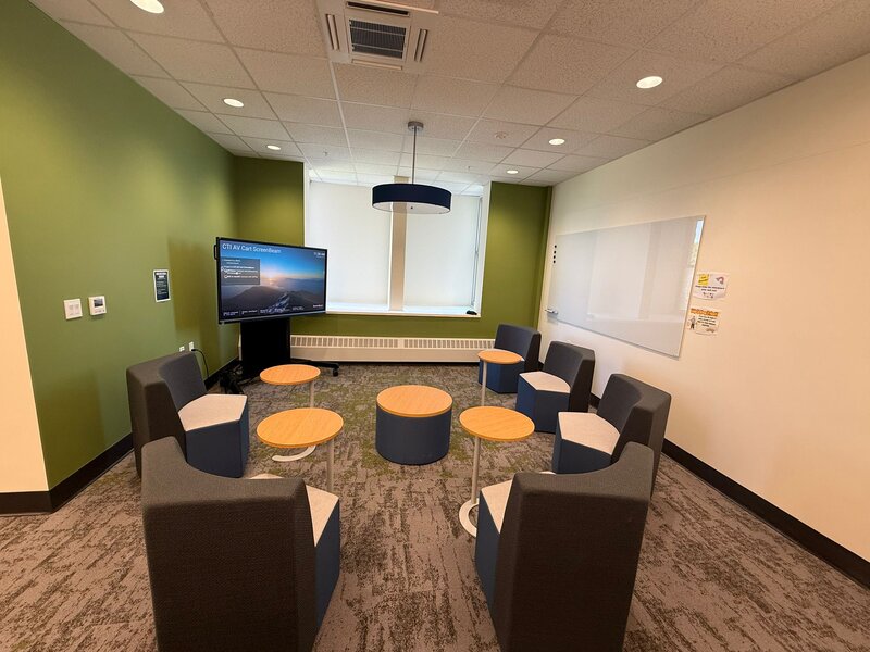 Huddle space with soft chairs, small tables, interactive screen and white board.