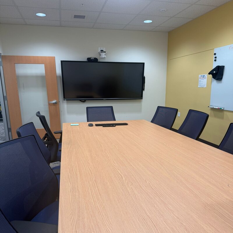 Conference room with a big table with many available chairs and a television to project on. 