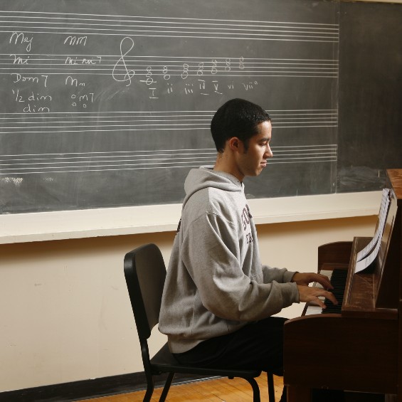 Student playing piano alone in classroom with blackboard behind them
