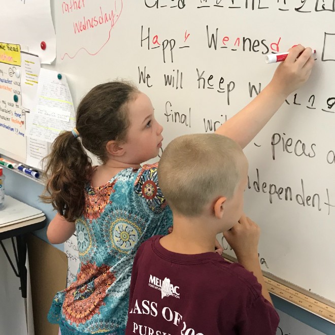 Students writing on a white board in a classroom