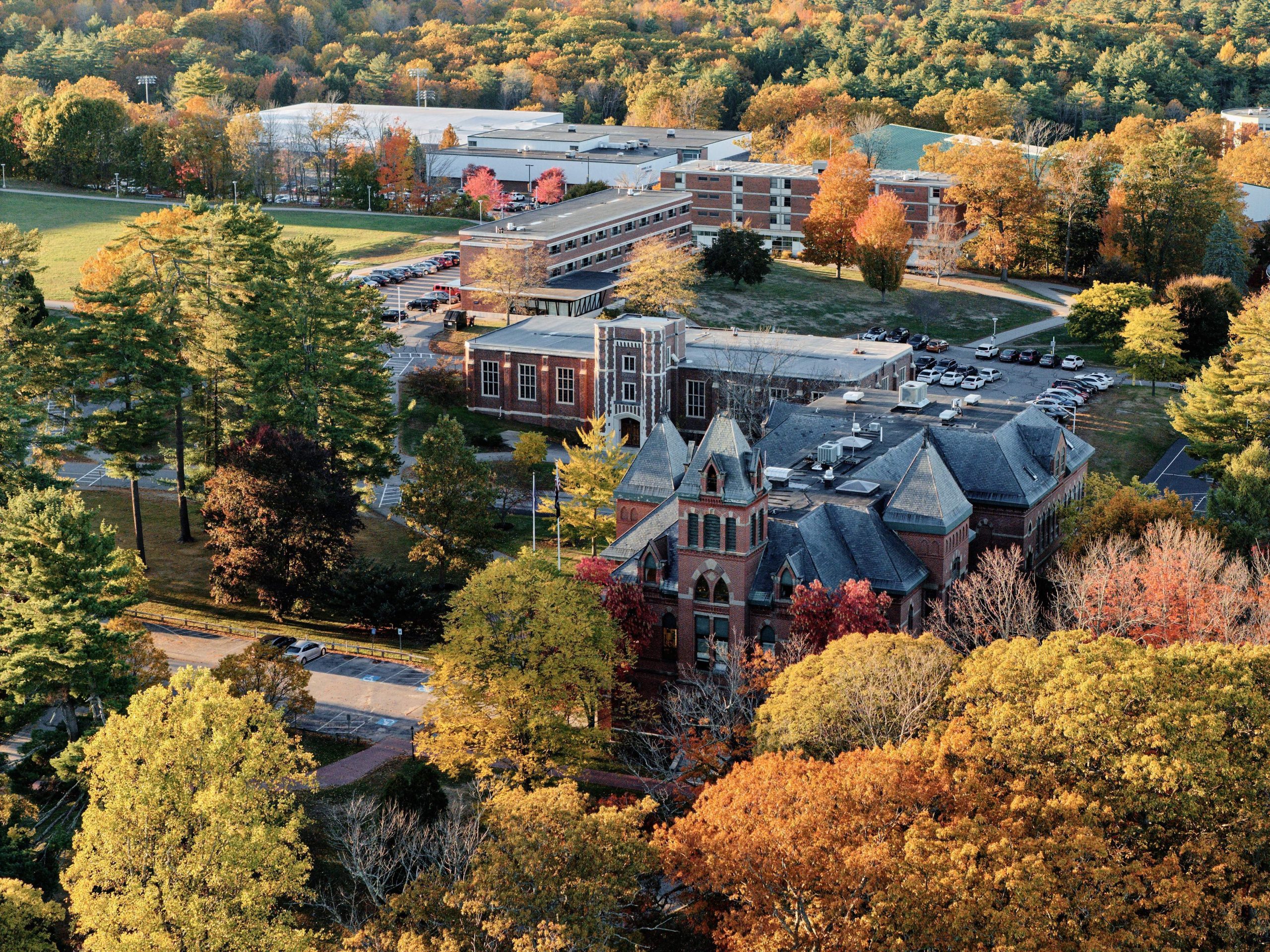 An aerial view of USM's Gorham campus in fall, with brick academic buildings nestled among trees displaying vibrant autumn foliage in shades of orange, red, yellow, and green.