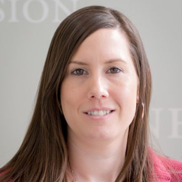 Professional headshot photo of Stacey Whitney. Stacey is wearing a pink colored sweater, has shoulder length brown hair and brown eyes.