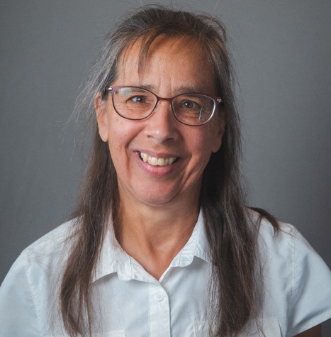 A woman with glasses and a white shirt smiling.