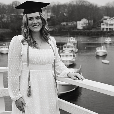 Taylor Brochu is on a platform with a peaceful boat-filled harbor in the background. 