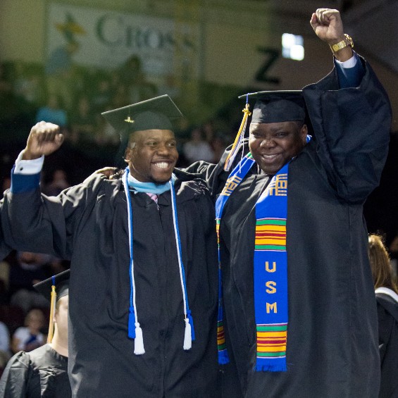Two USM graduates with arms raised in excitement