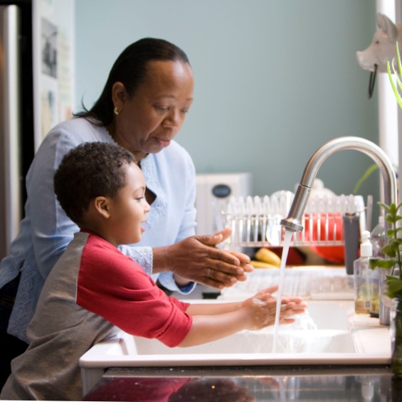 Grandmother and young grandson watching their hands at the kitchen sink