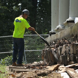 Workers remove a water-damaged section of foundation leading up to the front door of the Academy Building.