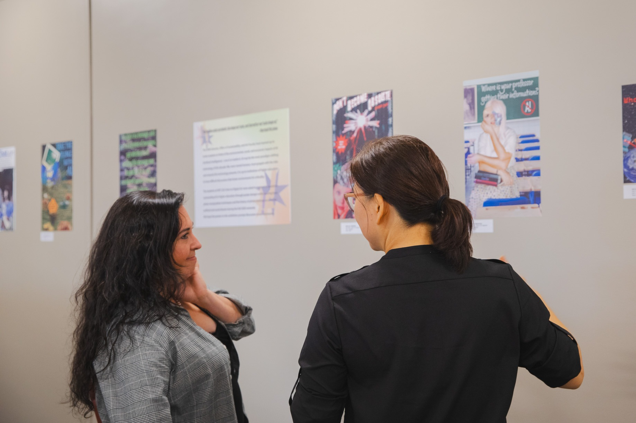Two visitors talk while viewing photo collage posters by ART 222 students at the Gorham Campus Library.