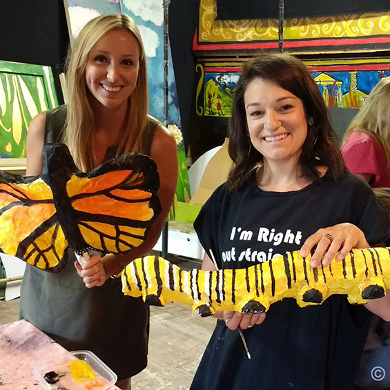 Two Art Ed students show off student made papermache caterpillar and butterfly