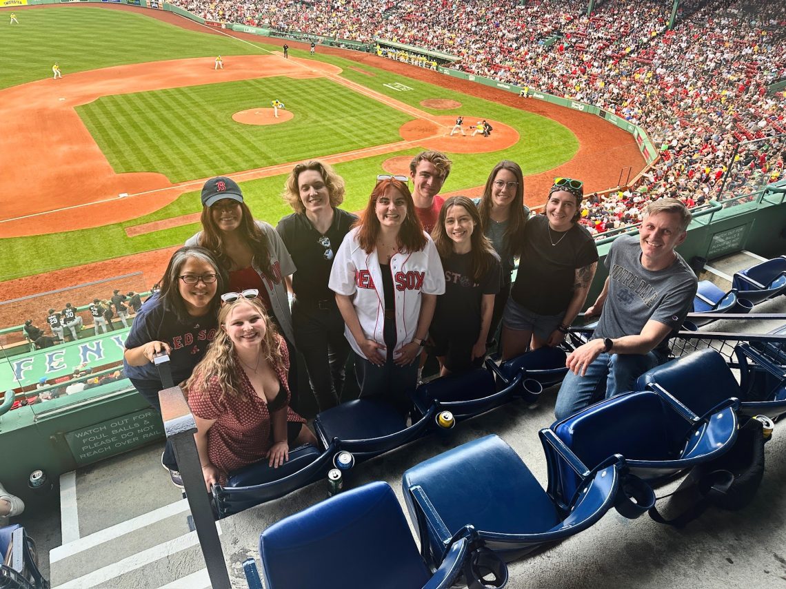 Students at a baseball stadium turned around to face the camera with the baseball diamond in the background.