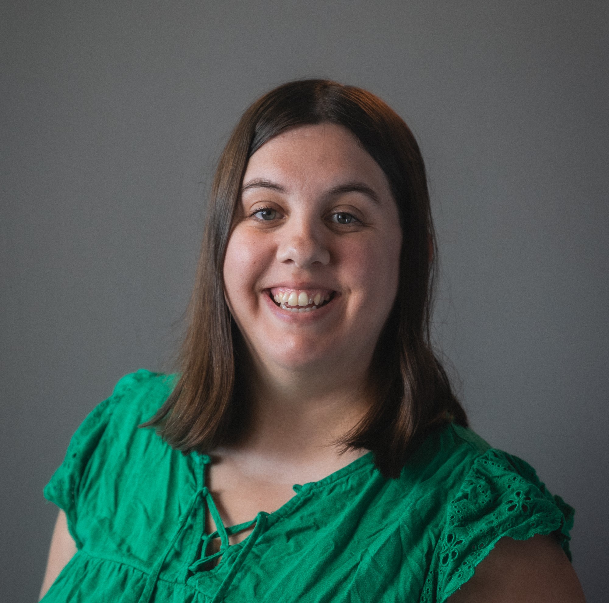 A headshot of Lindsay. She has shoulder length brown hair and a green top.