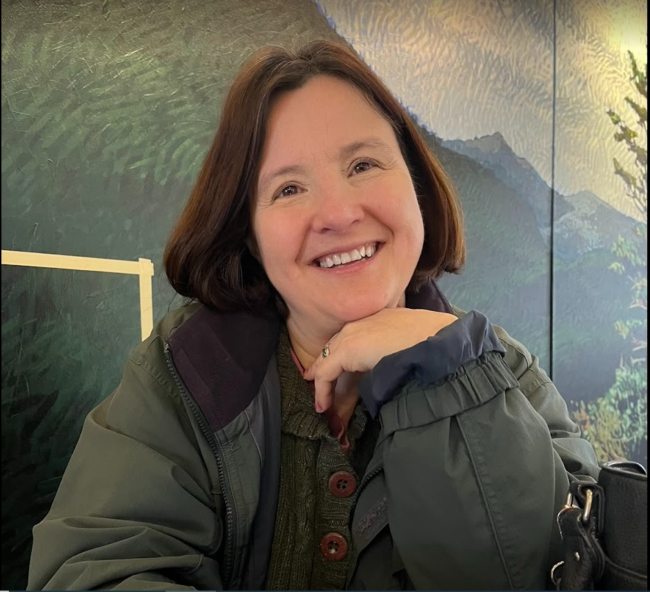 This is a photo of Katharine Thayer. She is wearing a green jacket, has short brown hair, and is smiling.
