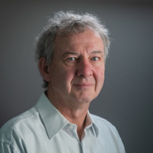 Headshot of a man with white hair wearing a white shirt with a gray background.