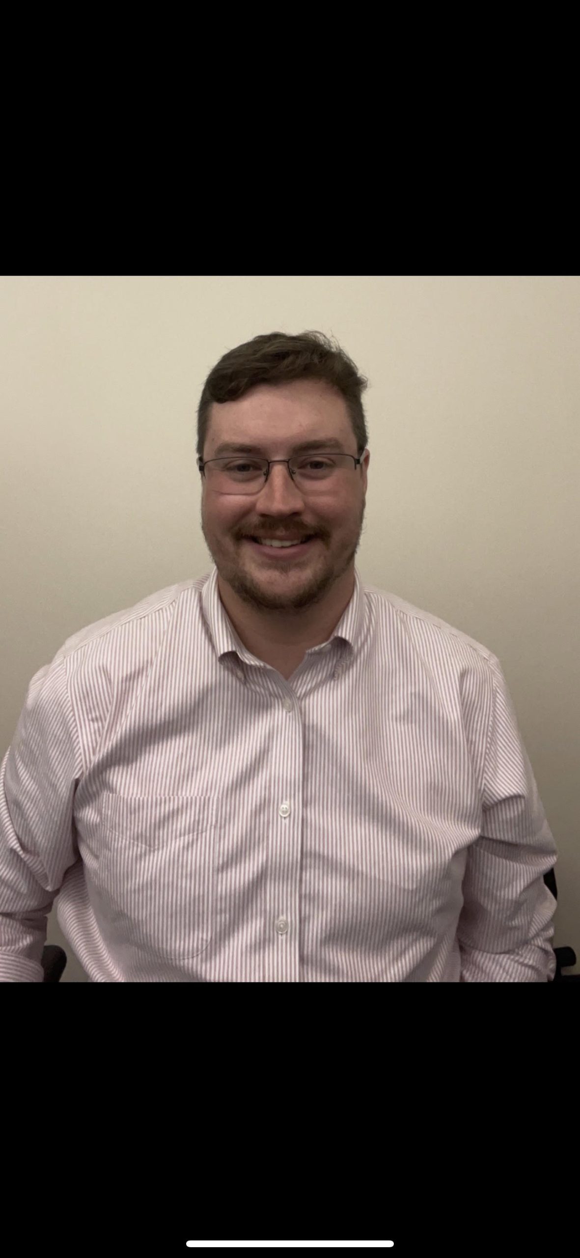 Tim is wearing glasses and a striped shirt and is smiling.